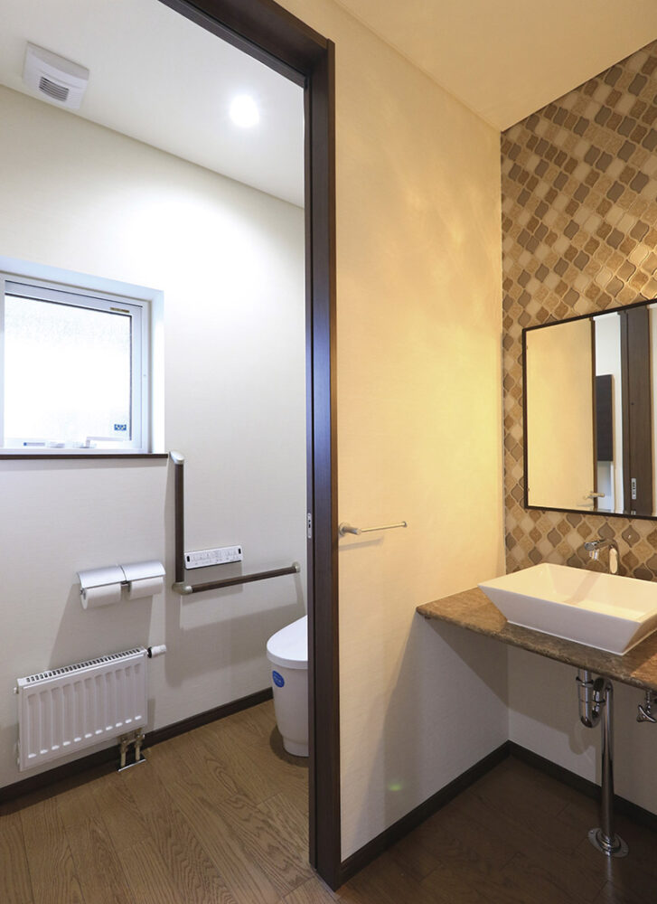 手すりも設置されたゆとりのあるトイレとデザインタイルが施された洗面スペース