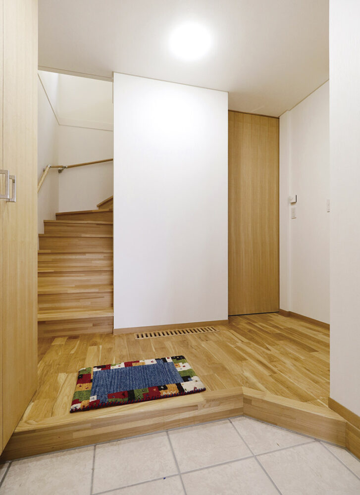 玄関土間には床暖房が設置され冬も暖かに家族を迎える。下駄箱とハイドアの建具はタモ無垢材を使用