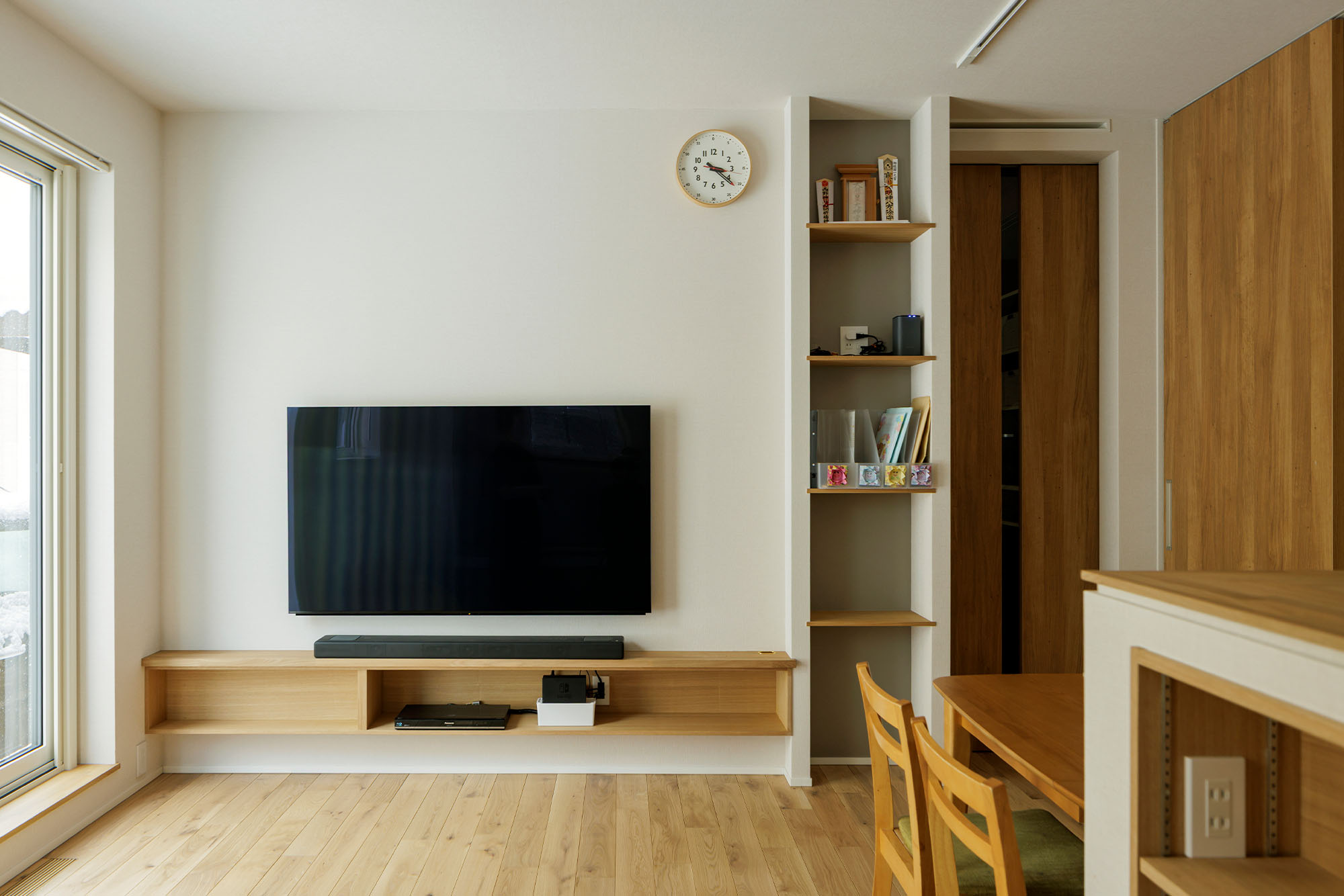ホコリがつきやすいテレビやチューナー類の配線を壁の中に隠せるつくりにし、テレビの下に横長のオープン収納を造作。テレビ横の収納は、子どもたちが持ち帰るプリント類が置ける奥行きで造りつけた。LDKの出入り口には、KAMIYAのフルハイトドアを採用した